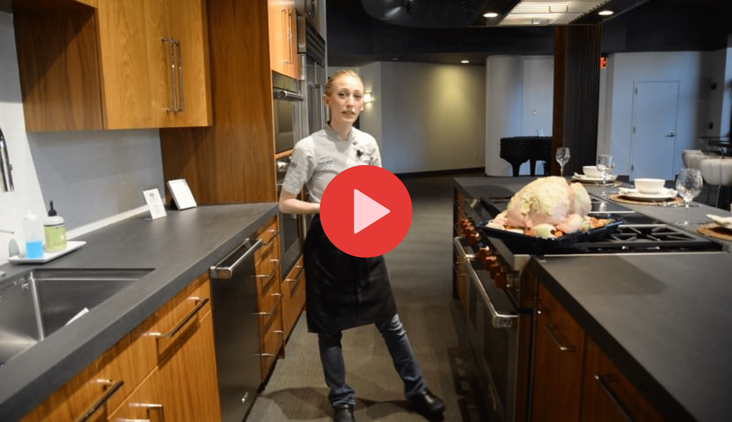 A chef stands in a modern kitchen showroom next to a raw turkey on a stove, surrounded by gleaming sub zero appliances and stylish cooking utensils on the counters.
