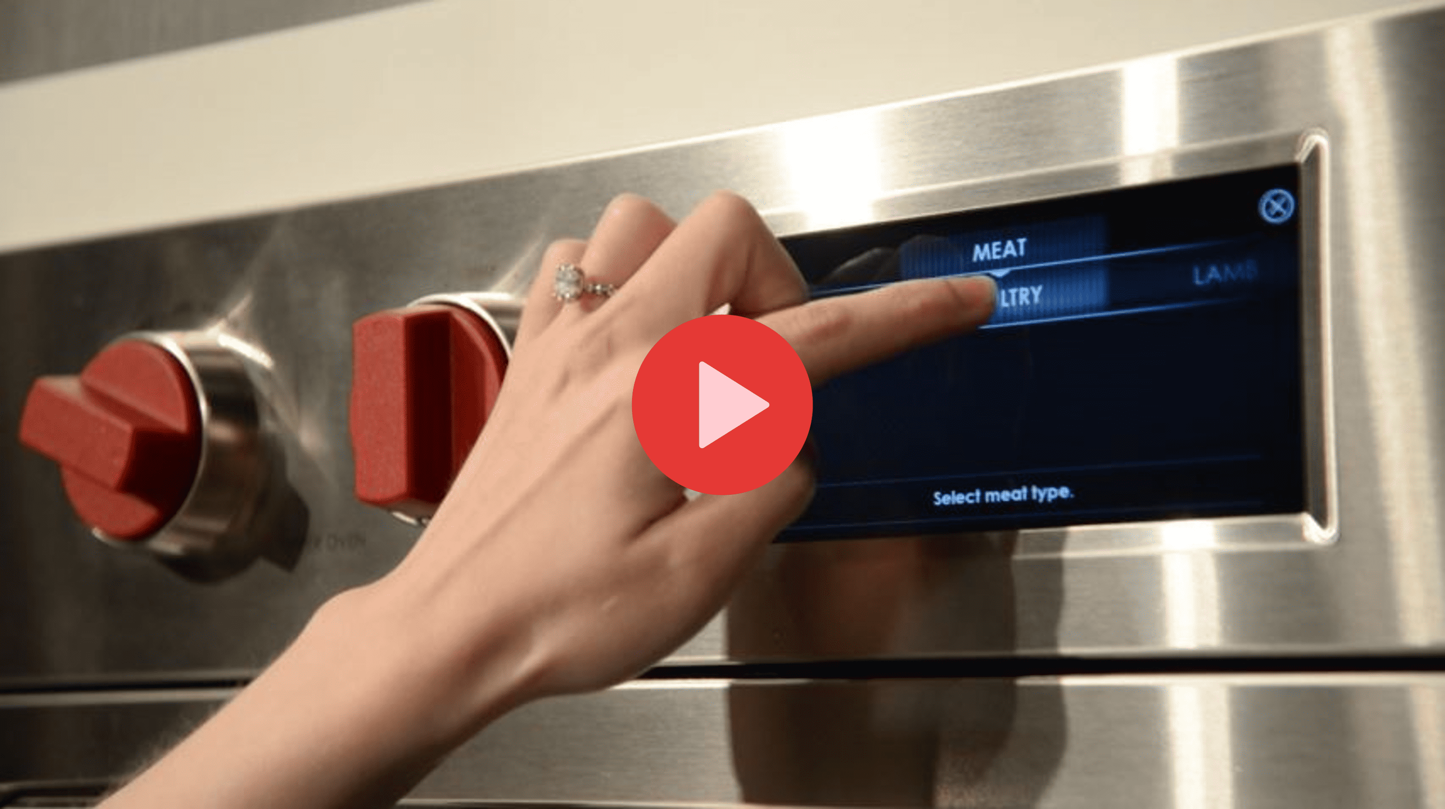 A hand with a ring selects "POULTRY" from a touchscreen menu on a sleek stainless steel oven, featuring red control knobs—an elegant sub zero appliance perfectly displayed in an upscale appliance showroom.