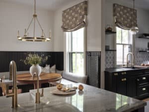 A modern kitchen with marble countertops, gold fixtures, a round wooden dining table with a vase of flowers, patterned window shades, and a sleek Sub Zero appliance for the ultimate luxury kitchen experience.