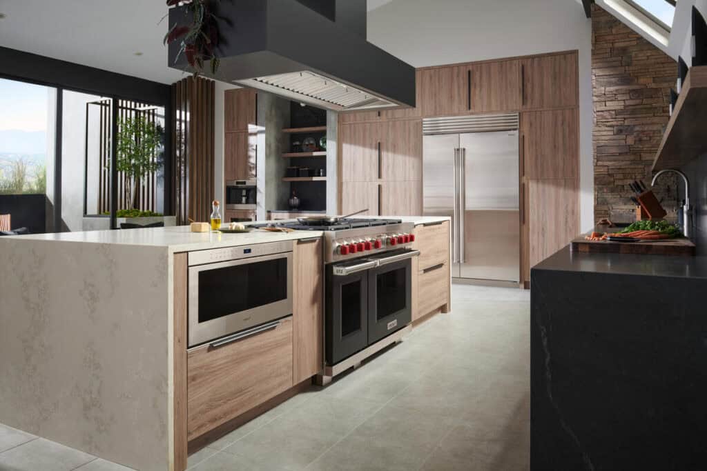 Modern kitchen with wood cabinets, a center island featuring a built-in microwave and oven, premium stainless steel appliances including Wolf appliance, and large windows providing natural light—perfect for a kitchen showroom.