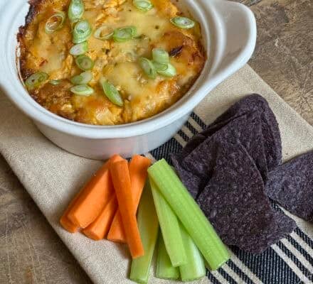 Spicy and creamy Buffalo Chicken Dip served in a bowl, garnished with green onions and surrounded by crispy tortilla chips, perfect for a game day snack or party appetizer