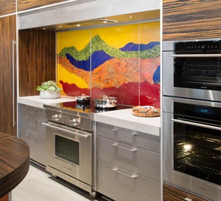 Modern kitchen with stainless steel appliances, wood-grain cabinets, and a backsplash featuring a colorful mountain landscape mural—perfect inspiration for your next visit to a high-end kitchen showroom.