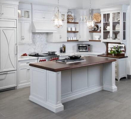 Modern white kitchen showroom with a central island, pendant lights, sub zero appliance, wolf appliance, open shelves, and glass-front cabinets.