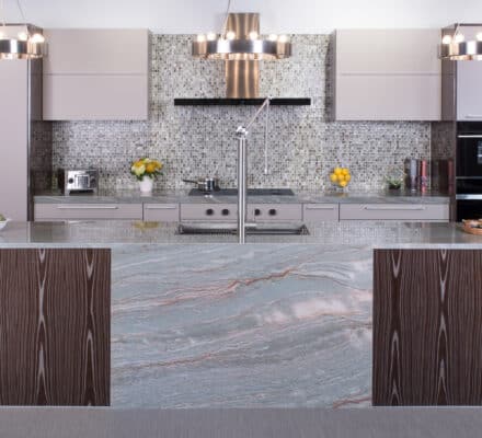 Modern kitchen with a large marble island, wood paneling, mosaic tile backsplash, Wolf appliances, and pendant lights—perfect for a high-end kitchen showroom.