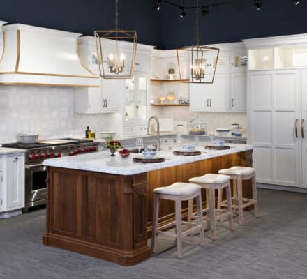 Modern kitchen with white cabinets, a wooden island with marble countertop, luxury kitchen appliances, three bar stools, and pendant lights hanging above the island—perfect for a kitchen showroom.